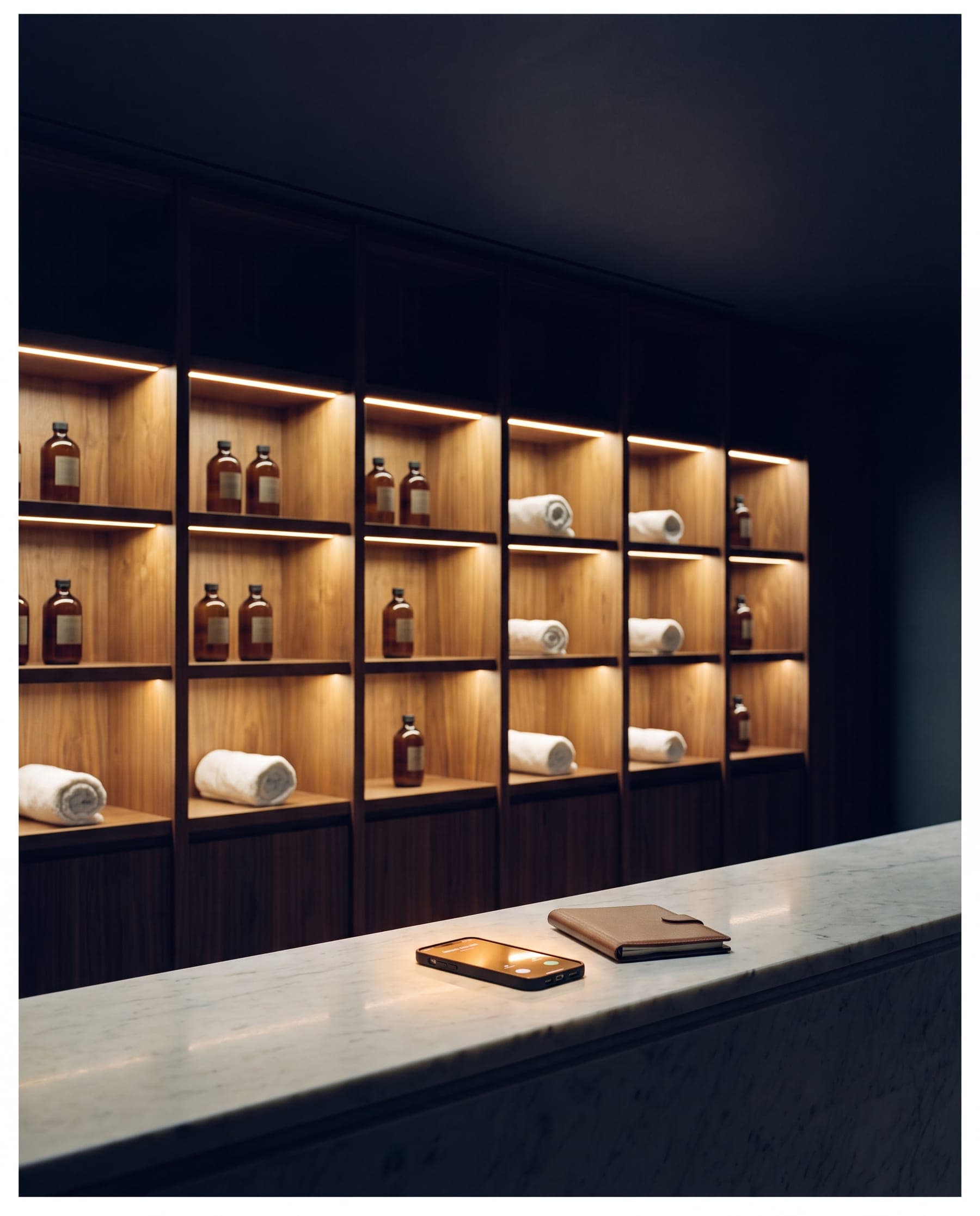 An empty spa reception counter at 2am, a phone glowing with an incoming call beside a closed folio